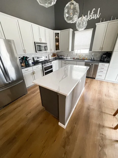 White kitchen cabinets, quartz island, stainless steel appliances, subway tile backsplash, wood flooring