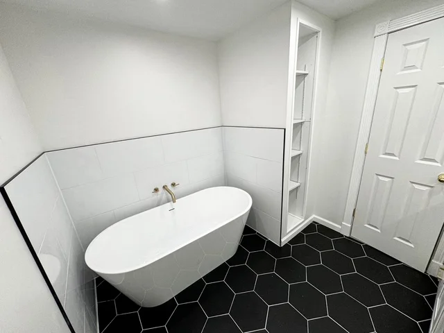 Freestanding white tub, white subway tile walls, black hexagonal floor tiles in modern bathroom