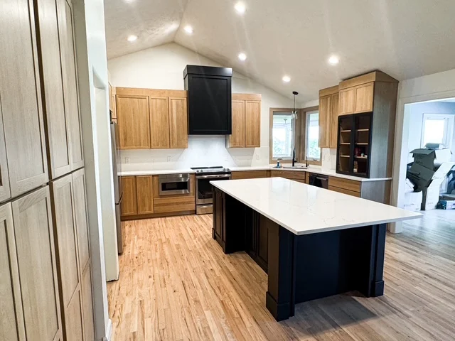 Modern kitchen with wood cabinetry, dark island, white countertops, and recessed lighting