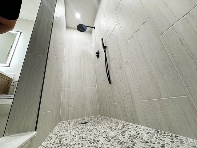 Walk-in shower with vertical gray tile walls, mosaic floor tile, and matte black fixtures
