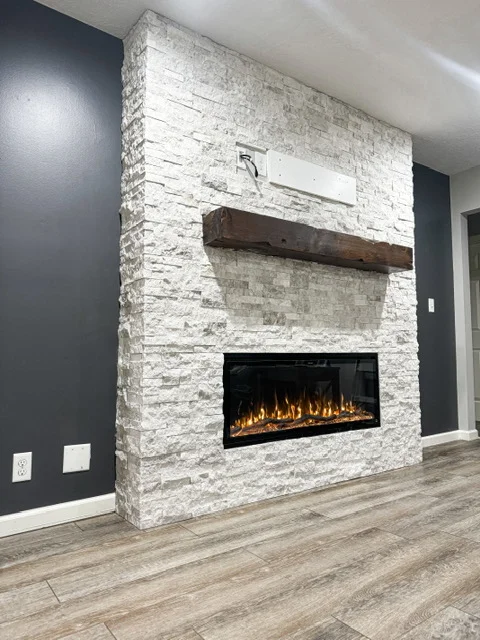 White stacked stone fireplace surround with electric insert and wood mantel shelf