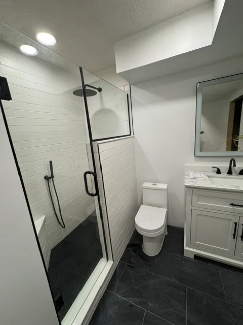 Modern bathroom with white subway tile shower, black floor tile, frameless glass enclosure, white vanity cabinet