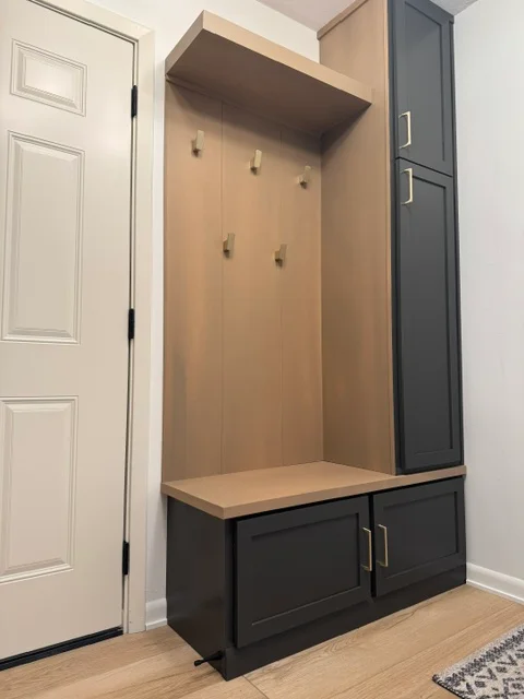 Black base cabinet with wood bench seat and tan wall-mounted shelving with brass hooks