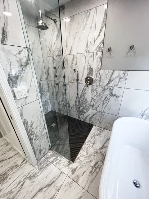 Marble tile shower with frameless glass door and black hexagonal floor tile