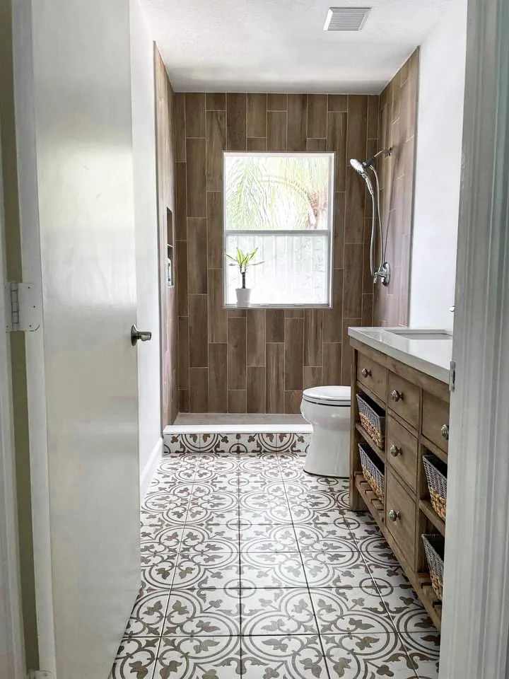 Bathroom with wood-look tile shower, patterned floor tiles, wooden vanity with baskets, and window niche