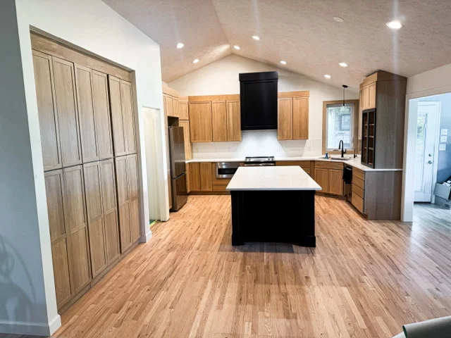 Modern kitchen with wood cabinetry, black island, white countertop, and vinyl plank flooring