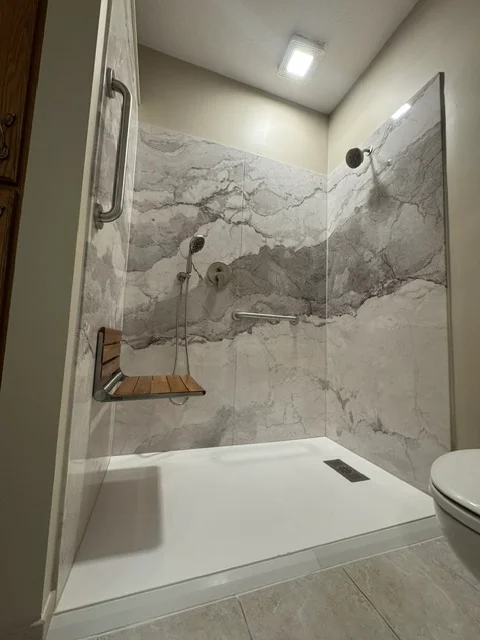 Marble tile shower enclosure with frameless glass door and white base pan