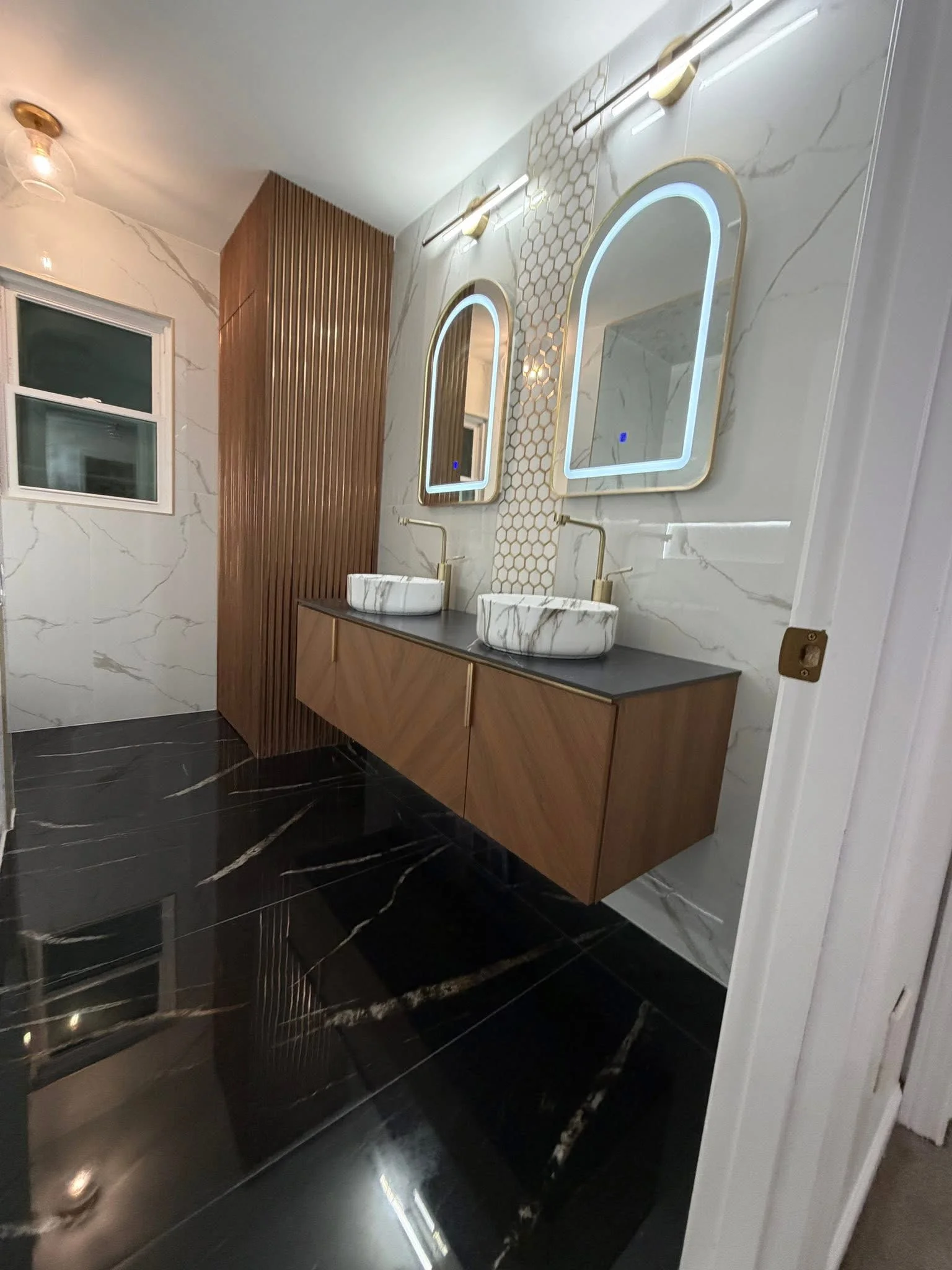 Modern bathroom with marble tile, walnut vanity, dual sinks, and LED mirrors