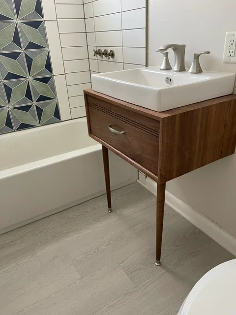Walnut vanity with vessel sink, geometric tile shower surround, and gray wood-look flooring