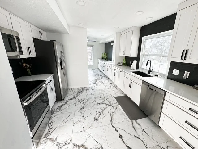White kitchen cabinets, black backsplash, marble flooring, stainless steel appliances