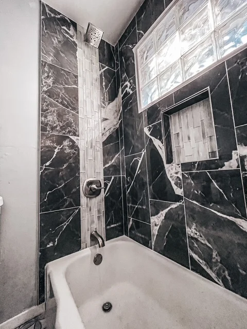 Black marble tile shower surround with white veining and geometric layout