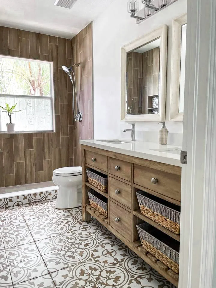 Bathroom with wood-look tile shower, wooden vanity with baskets, patterned floor tile, and framed mirror