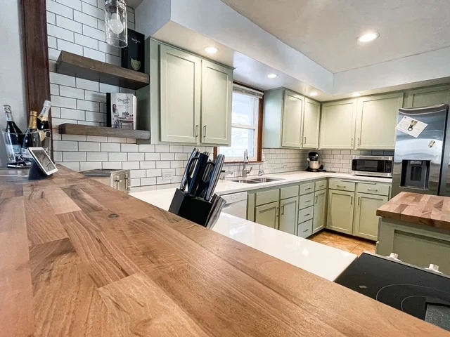 Sage green kitchen cabinets, white subway tile backsplash, wood countertops, stainless steel appliances