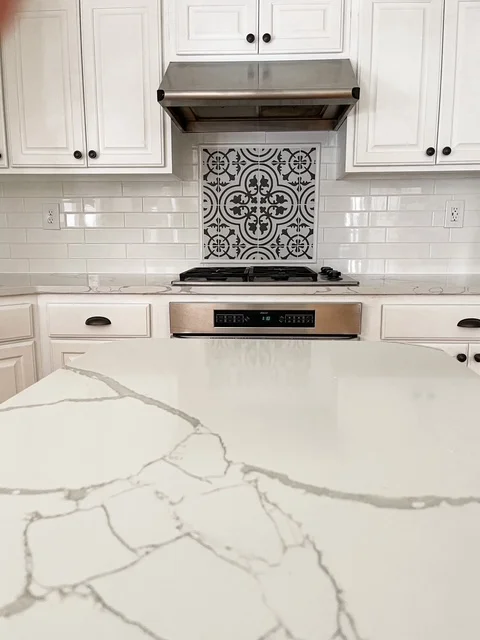 White kitchen with geometric patterned tile backsplash, quartz counters, and stainless steel appliances
