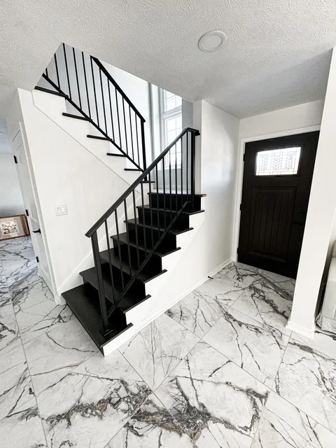 Marble tile flooring with gray veining in entryway, black metal staircase with vertical railings