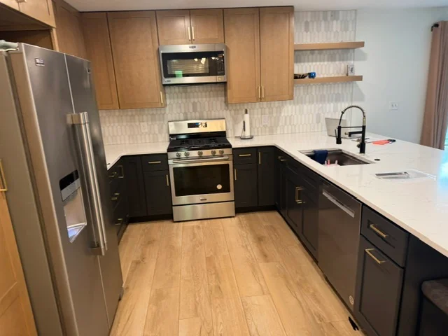 Kitchen with two-tone cabinets, stainless steel appliances, geometric tile backsplash, and wood flooring