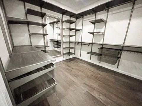 Custom wood shelving unit installed floor-to-ceiling along a finished wall inside a Lincoln, NE home, with evenly spaced shelves anchored to wall framing and a painted finish matching the room trim. The shelving spans a closet alcove and holds neatly organized household items.